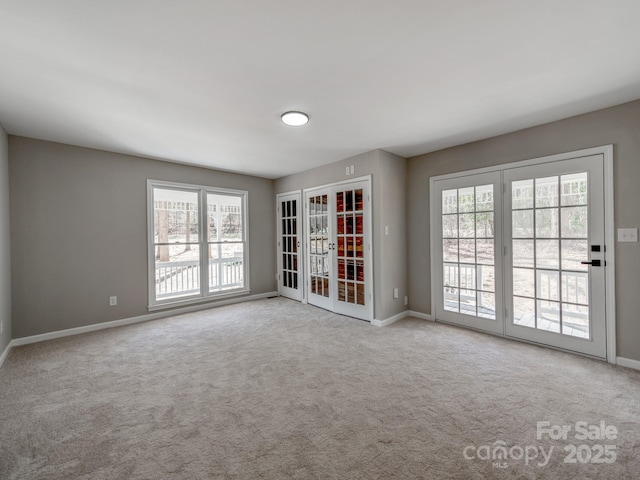 carpeted spare room featuring french doors and baseboards