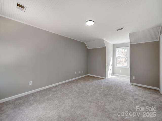 carpeted spare room with visible vents, vaulted ceiling, and baseboards