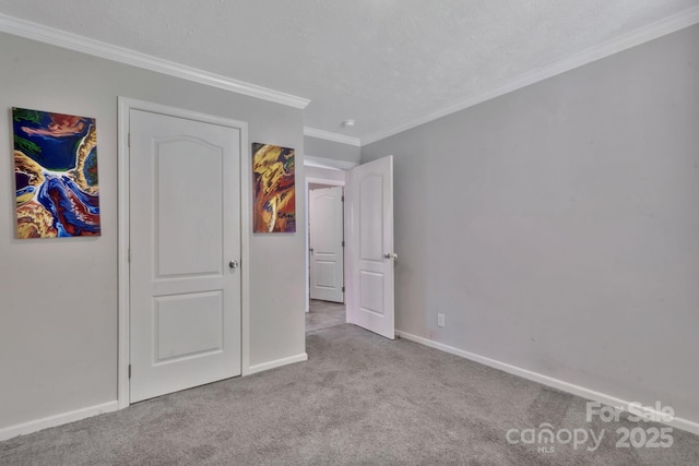 unfurnished bedroom with a textured ceiling, carpet floors, ornamental molding, and baseboards