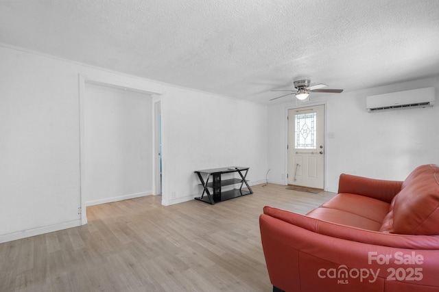 living room with a wall mounted air conditioner, a ceiling fan, a textured ceiling, wood finished floors, and baseboards