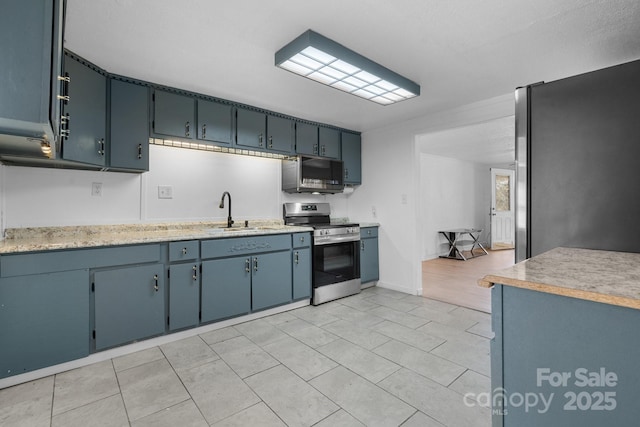 kitchen with a sink, blue cabinetry, appliances with stainless steel finishes, light countertops, and light tile patterned floors