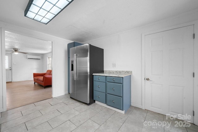 kitchen with blue cabinets, a ceiling fan, a wall mounted AC, stainless steel fridge, and light countertops