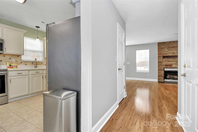 kitchen featuring decorative light fixtures, stainless steel electric range oven, a fireplace, light countertops, and baseboards