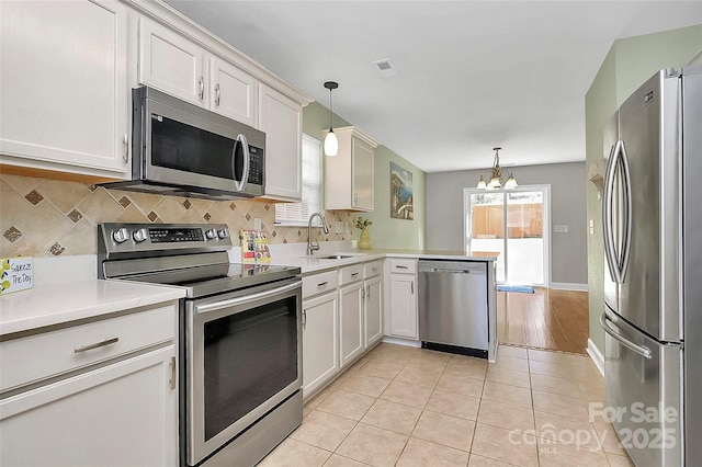 kitchen with decorative backsplash, a peninsula, stainless steel appliances, light countertops, and a sink