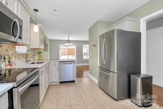 kitchen with appliances with stainless steel finishes, light countertops, a sink, and hanging light fixtures