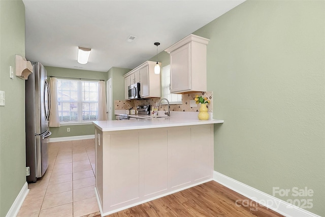 kitchen featuring stainless steel appliances, tasteful backsplash, light countertops, a sink, and a peninsula