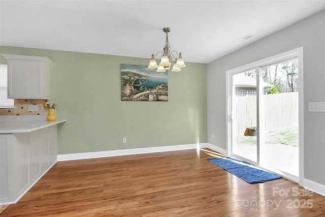 unfurnished dining area with visible vents, light wood-style flooring, baseboards, and an inviting chandelier