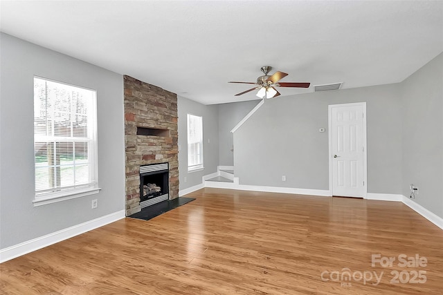 unfurnished living room featuring ceiling fan, a fireplace, visible vents, baseboards, and light wood-style floors