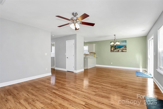 unfurnished living room featuring light wood finished floors, baseboards, and ceiling fan with notable chandelier