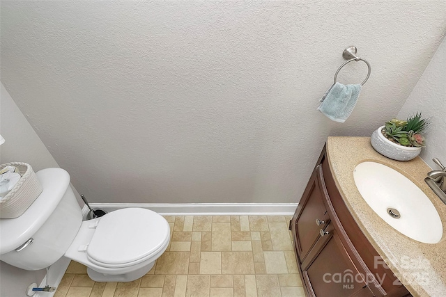 half bathroom with a textured wall, vanity, and toilet