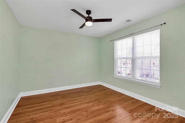 empty room with a ceiling fan, visible vents, baseboards, and wood finished floors