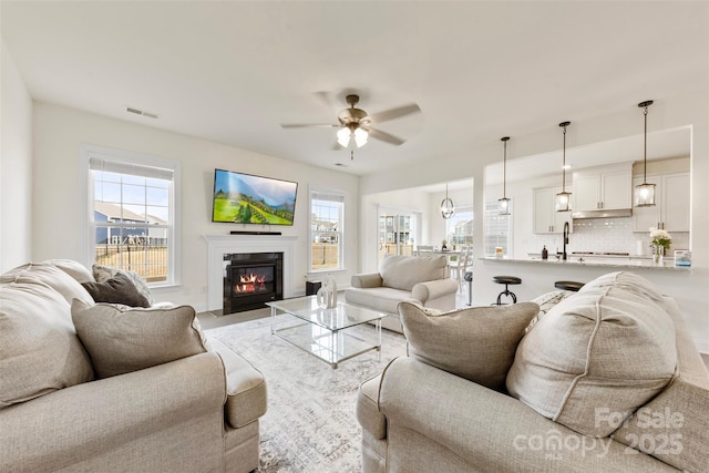 living room featuring a glass covered fireplace, a healthy amount of sunlight, ceiling fan, and visible vents