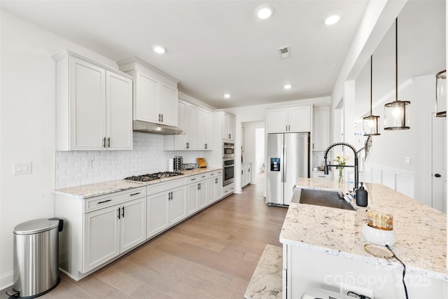 kitchen featuring tasteful backsplash, visible vents, appliances with stainless steel finishes, a sink, and under cabinet range hood