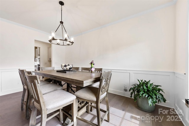 dining space featuring a wainscoted wall, ornamental molding, wood finished floors, and an inviting chandelier