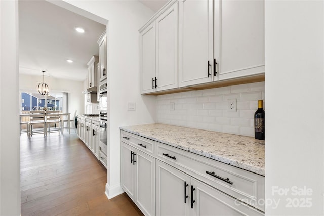 kitchen with light stone counters, recessed lighting, wood finished floors, white cabinetry, and backsplash