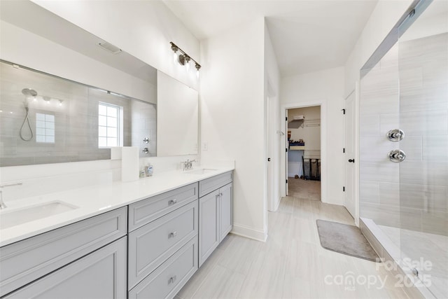 full bath featuring a walk in closet, a sink, a tile shower, and double vanity