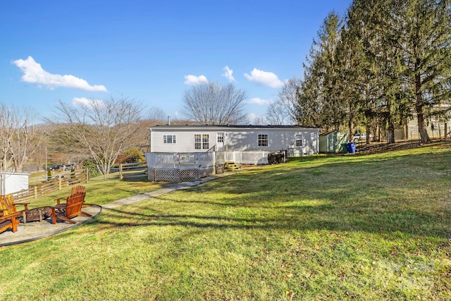 back of property featuring a fire pit, fence, a lawn, and a wooden deck