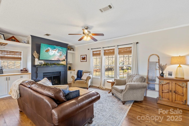 living area featuring light wood-style floors, visible vents, a fireplace with raised hearth, and ornamental molding