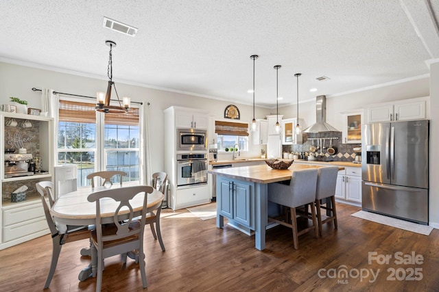 kitchen featuring stainless steel appliances, visible vents, wooden counters, white cabinets, and wall chimney exhaust hood