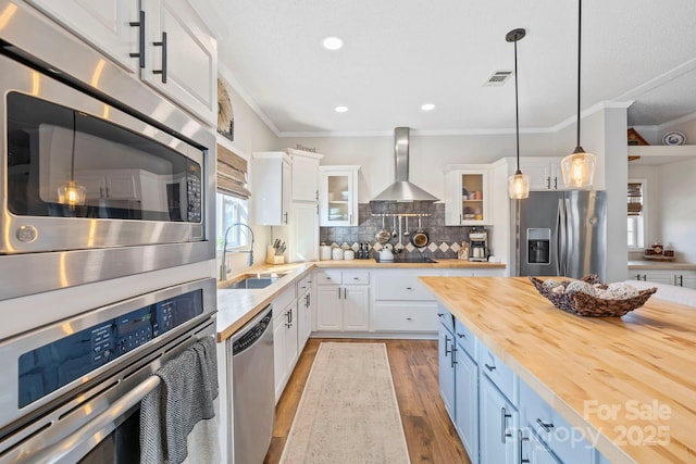 kitchen with visible vents, wooden counters, appliances with stainless steel finishes, a sink, and wall chimney range hood