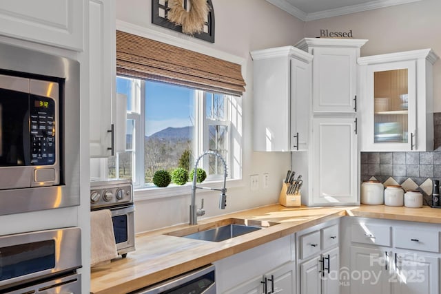 kitchen with butcher block countertops, white cabinetry, a sink, and tasteful backsplash