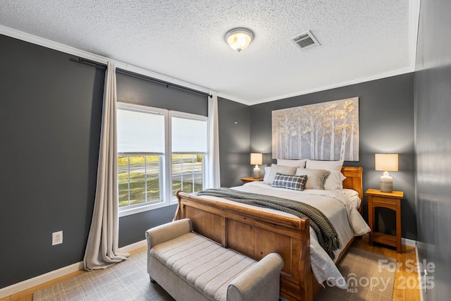 bedroom with baseboards, a textured ceiling, visible vents, and wood finished floors