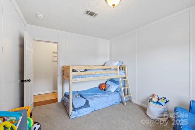 bedroom featuring carpet floors, visible vents, crown molding, and a textured ceiling