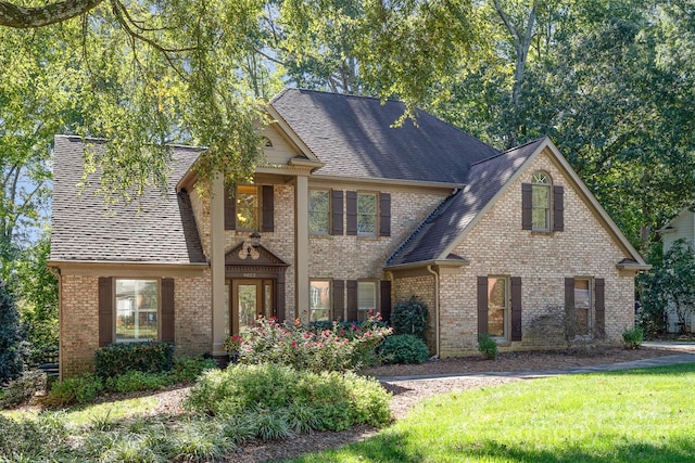 view of front of property featuring brick siding, a shingled roof, and a front yard