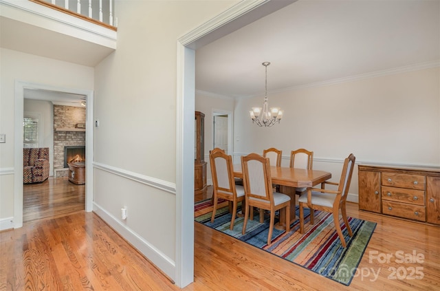 dining area with baseboards, light wood-style flooring, ornamental molding, a stone fireplace, and a chandelier