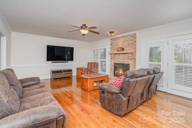 living area featuring ceiling fan, light wood-style flooring, a fireplace, and ornamental molding