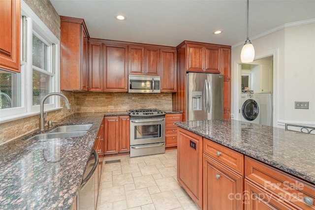 kitchen with washer / clothes dryer, a sink, stainless steel appliances, pendant lighting, and tasteful backsplash