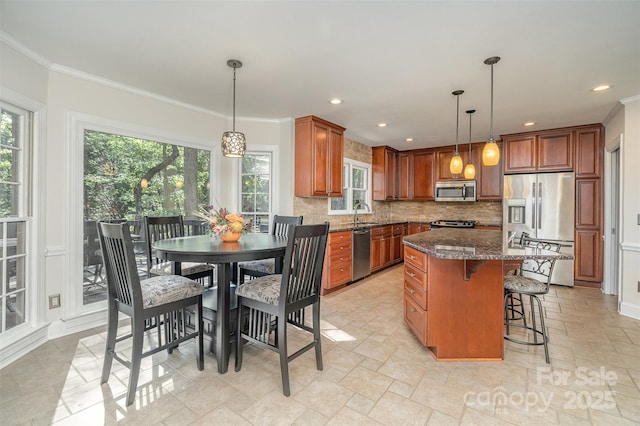 kitchen with brown cabinetry, a kitchen island, ornamental molding, appliances with stainless steel finishes, and tasteful backsplash