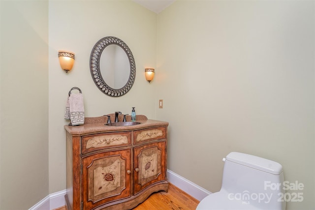 half bathroom featuring baseboards, toilet, wood finished floors, and vanity