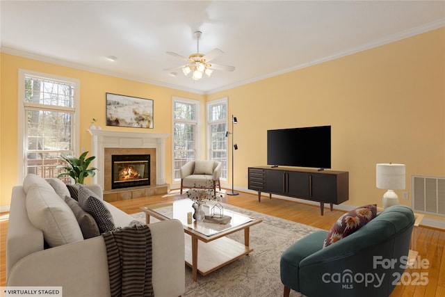 living room with wood finished floors, visible vents, a fireplace, ceiling fan, and ornamental molding