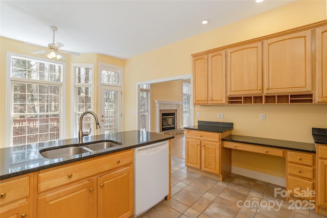 kitchen with light brown cabinetry, dishwasher, dark stone counters, a ceiling fan, and a sink