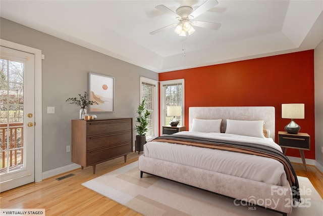 bedroom featuring a raised ceiling, light wood-style flooring, visible vents, and baseboards