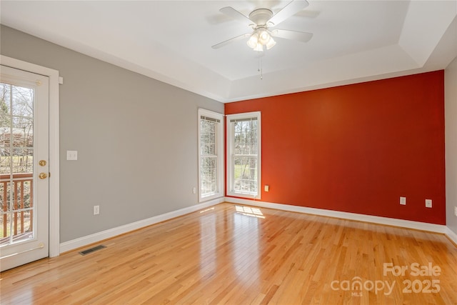 empty room with ceiling fan, baseboards, a raised ceiling, and light wood-style flooring