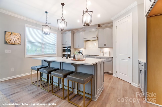 kitchen with a center island with sink, light countertops, ornamental molding, appliances with stainless steel finishes, and a kitchen bar