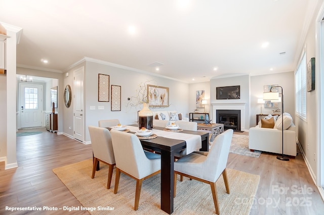 dining space featuring light wood-style floors, a fireplace with flush hearth, ornamental molding, and baseboards