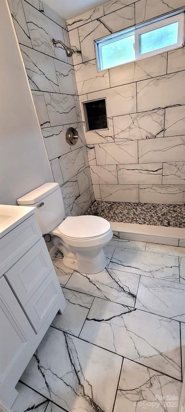 full bath featuring toilet, marble finish floor, tiled shower, and vanity