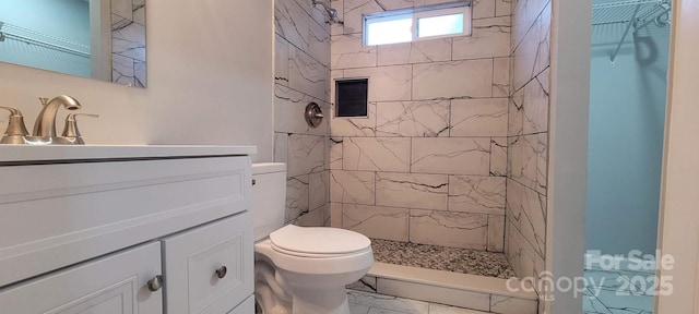 bathroom featuring toilet, marble finish floor, a tile shower, and vanity