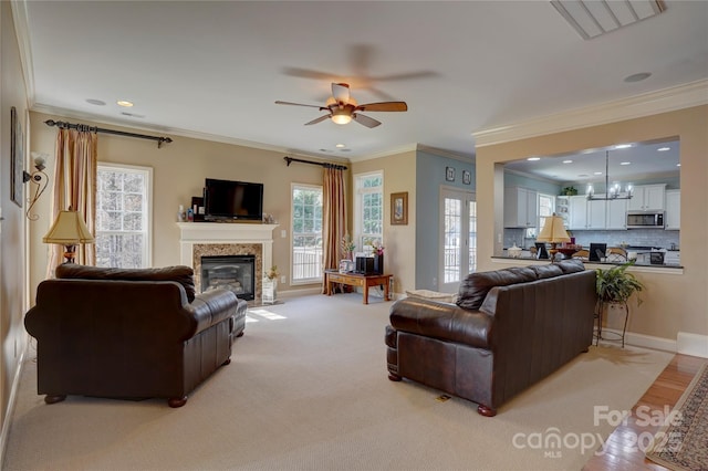 living room with visible vents, a fireplace with flush hearth, crown molding, and ceiling fan with notable chandelier