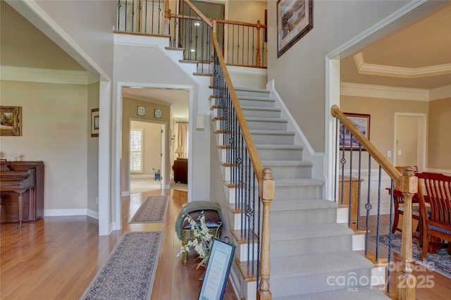 stairs featuring crown molding, wood finished floors, baseboards, and a towering ceiling