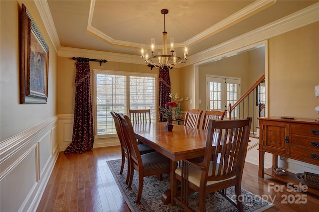 dining area featuring a chandelier, a tray ceiling, hardwood / wood-style floors, wainscoting, and a decorative wall