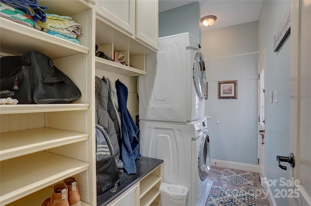 clothes washing area featuring baseboards, cabinet space, and stacked washer and clothes dryer