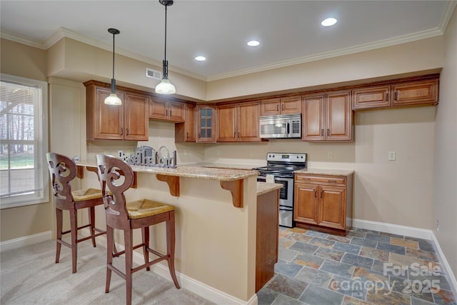 kitchen with a peninsula, light stone counters, brown cabinets, and stainless steel appliances