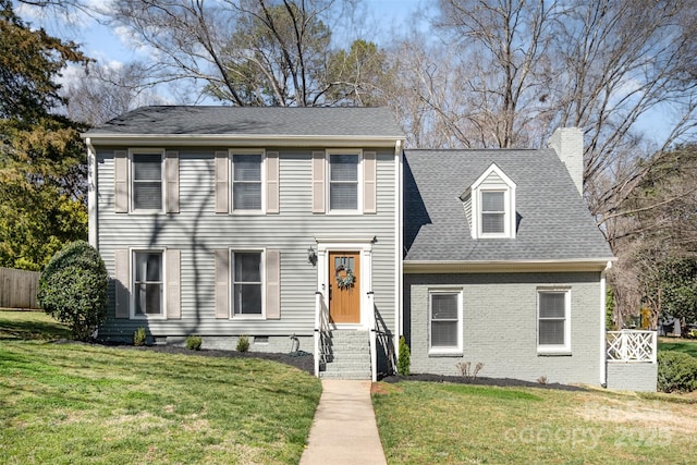 colonial-style house featuring a shingled roof, a chimney, a front lawn, crawl space, and brick siding