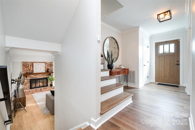 entryway with visible vents, light wood finished floors, crown molding, a fireplace, and stairs