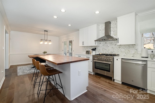 kitchen featuring white cabinetry, appliances with stainless steel finishes, crown molding, wall chimney range hood, and wooden counters