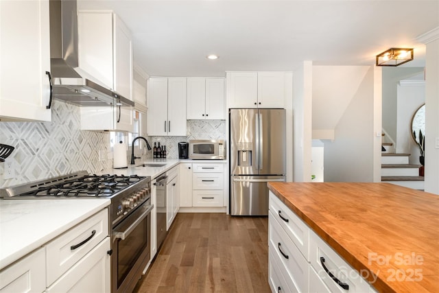 kitchen featuring butcher block countertops, a sink, appliances with stainless steel finishes, wall chimney range hood, and dark wood-style flooring